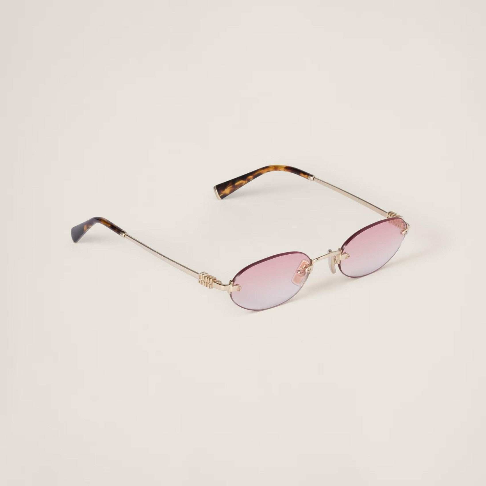 Oval sunglasses with pinkish-red lenses, gold metal frame, and adjustable nose pads.
