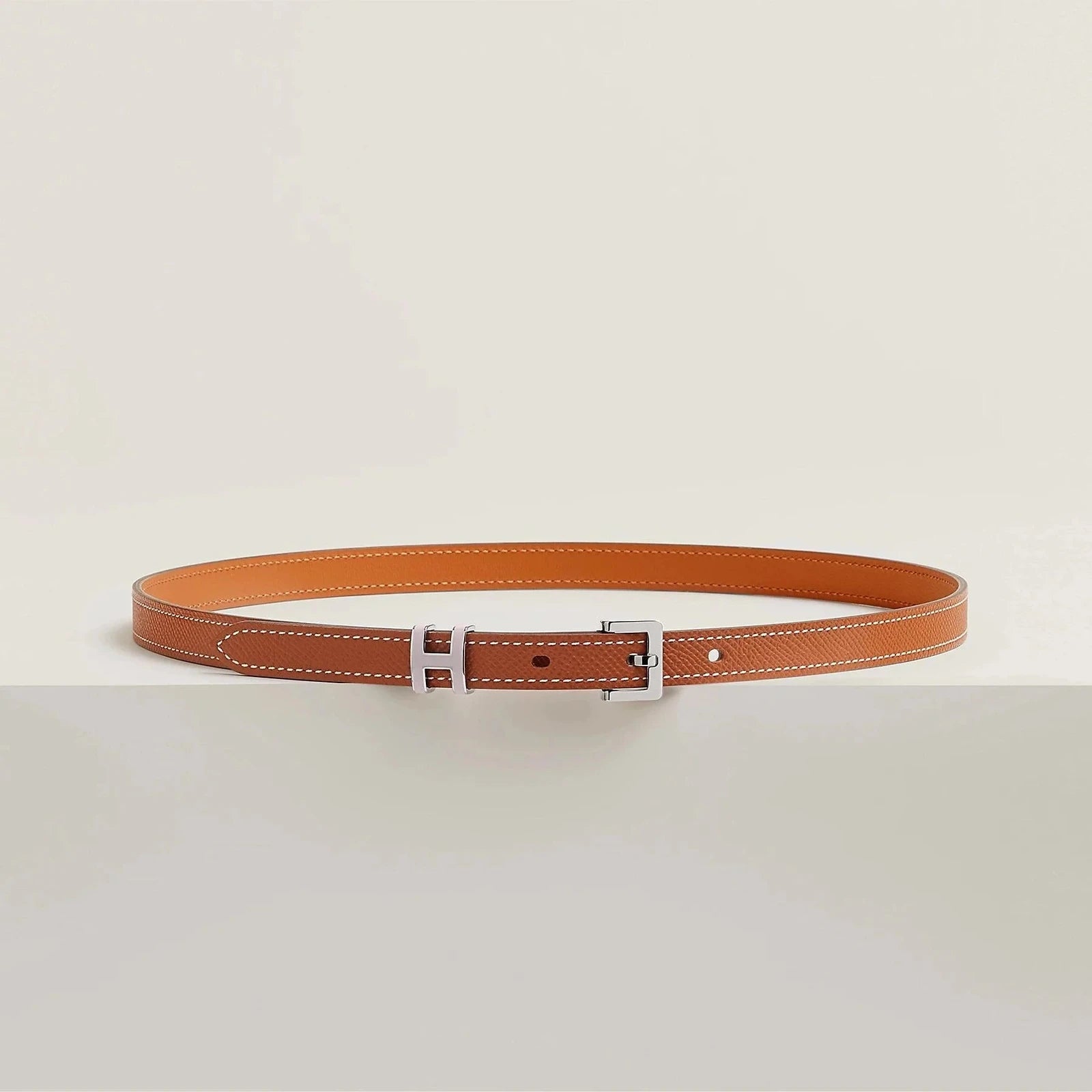 Image of Luxurious Hermes leather belt with sleek metallic buckle on a minimalist design.
